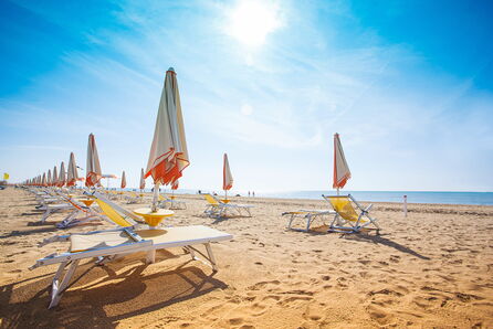 Sonnenschirme und Liegen an einem Sandstrand mit Blick auf das blaue Meer